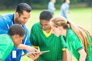 Halftime of a soccer game with kids in green jerseys and coach with a clipboard